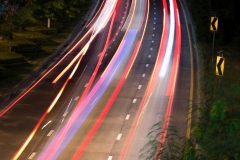 Bend in the road with long exposure and highway that curves to the right.  Cars coming in both directions at night, illuminating the roadway with street lights.