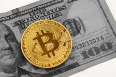 Golden bitcoin on black and white hundred dollar bill with white background.