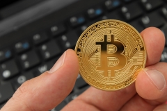 Holding a bitcoin digital currency with laptop in background.