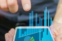 Hand pointing at mobile device for business use and charting data with bar charts and pie chart and valueable information on the company financial network.