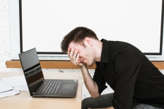 Man with headache in office on laptop.  Closed eyes and deep in thought.