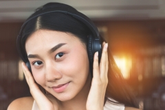 Streaming music online.  Happy asian girl listening to new songs and audio on headphones.